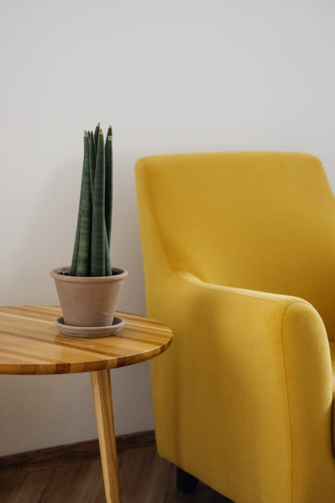 The Art of Drawing Readers In: Your attractive post title goes here Creative composition of comfortable yellow armchair with soft cushion and round wooden table with green home plant in pot against white wall in light apartment or flat with wooden floor
